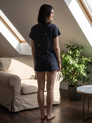 A woman in navy blue celestial print pajama shorts and t-shirt stands facing away from the camera.