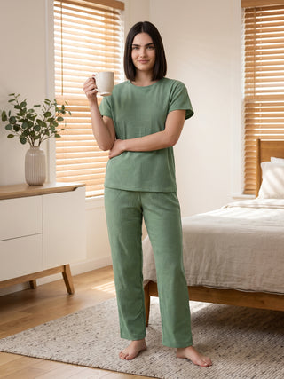 A woman stands in a green pajama set with a geometric print, holding a mug.