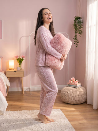 A woman in pink patterned pajamas stands holding a fluffy pink pillow.