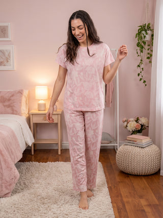 A woman in a pink floral pajama set walks through a bedroom.