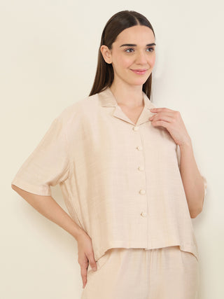 A woman in a beige short-sleeve pajama set stands posing, with her hands on her hips.