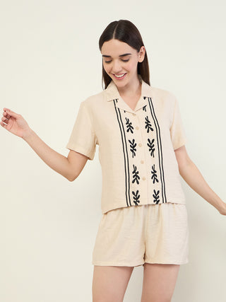 A woman poses in a light beige linen sleep set with a black embroidered print.