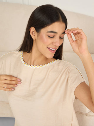 Women wearing a beige daisy-trimmed sleepwear top, posing looking down and to the side, with one hand touching her forehead, a contrast to the previous image where she is looking straight at the camera.