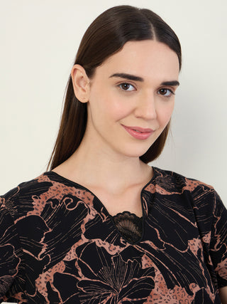 A woman poses with her head tilted slightly, wearing a black and brown floral printed sleepwear top with a lace trim detail.