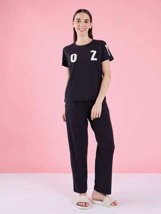 Women's black short-sleeve t-shirt with white "OZ" print and matching black pajama pants, posed standing.