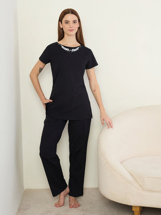 A woman stands posing in black, short-sleeved sleepwear with a laurel leaf print around the neckline.