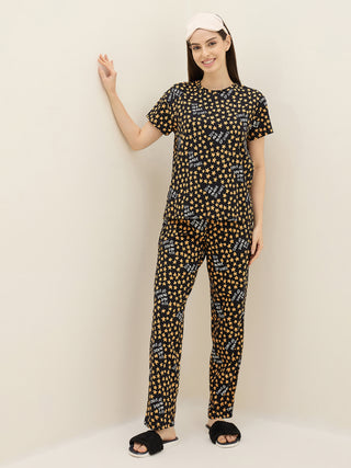 A woman poses in a black short-sleeved pajama set with a yellow star print and a pink sleep mask.