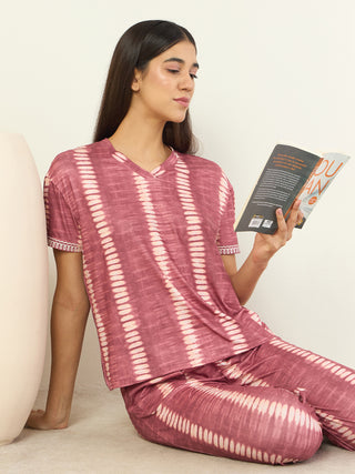 A woman wearing a pink tie-dye pajama set sits on the floor reading a book.