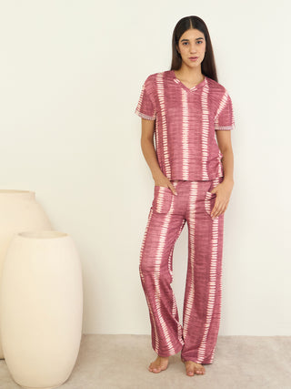Women's pink tie-dye pajama set, standing with hands in pockets, with cream vases in the background.