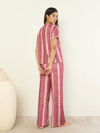 Women in a pink tie-dye pajama set, posing with hands clasped behind their backs, with a white background and a beige vase.
