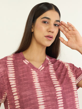 A woman in a pink tie-dye sleep shirt looks forward as she rests her hand on her forehead.
