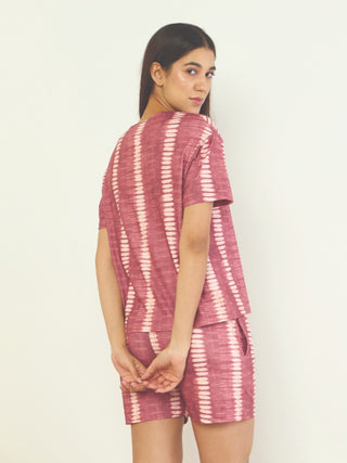 A young woman poses with her hands clasped behind her back, wearing a burgundy tie-dye printed pajama set.