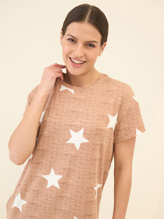 A woman poses wearing a tan t-shirt with white stars.