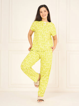 A woman stands on one leg, wearing a lime green pajama set with a white bear-shaped print and fuzzy slippers.