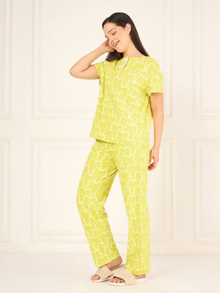 A woman in a lime green pajama set with a white bear print poses with her hand on her head, smiling.