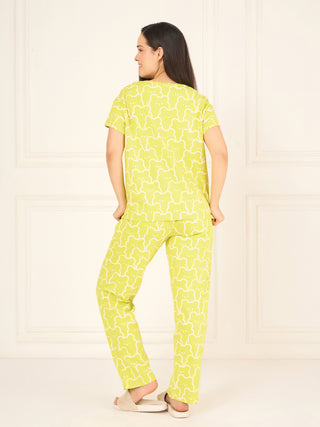 A woman, facing away from the camera, is modeling a lime green pajama set with a white teddy bear print, different from the previous image in that she is wearing slippers.