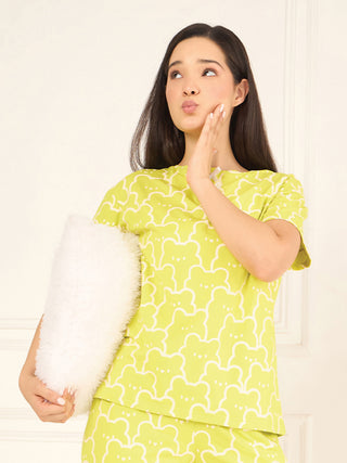 A woman, facing away from the camera, is modeling a lime green pajama set with a white teddy bear print.