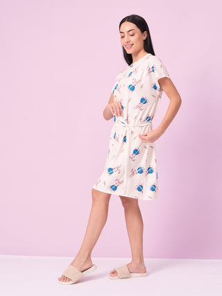 Woman standing in a relaxed walking pose, wearing a cream short-sleeve knee-length sleep dress with a waist tie and an all-over pink-and-blue bunny print.