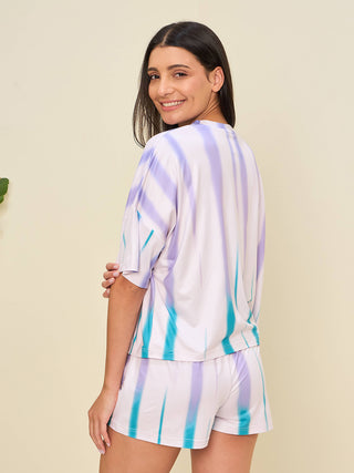 A woman is posing in a white tie-dye pajama set with purple and turquoise stripes.