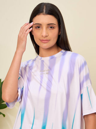 A woman poses with her hand touching her forehead, wearing a tie-dye t-shirt with purple and teal stripes, which reads "Forever Offline".