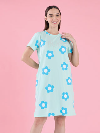 A woman is posing in a light blue t-shirt dress with a floral print.