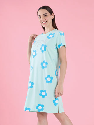 A young woman poses playfully in a light blue, short-sleeved sleep dress adorned with a repeating blue flower pattern and "DREAM" written in rhinestones on the chest.