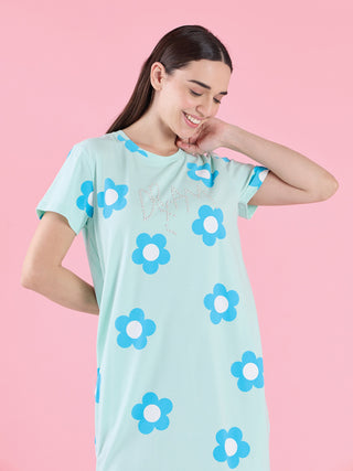 Women, smiling and looking down while wearing a light mint green, short-sleeved sleep dress with blue and white flowers and "DREAM" text.