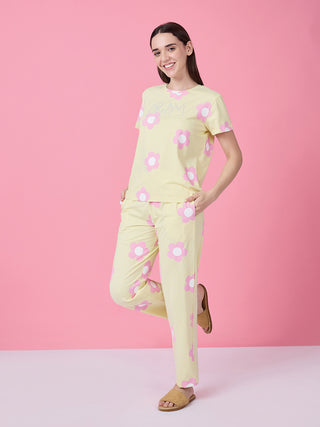 Women in a light yellow pajama set with pink flowers and "DREAM" printed on the top, standing with one leg bent.