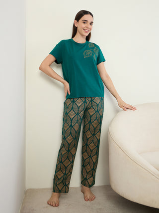 Women in a full body pose wearing a teal t-shirt with gold leaf print and matching teal pants with a gold diamond pattern.