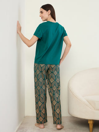 Women in a green t-shirt and patterned green and gold pajama pants, standing with their back to the camera.