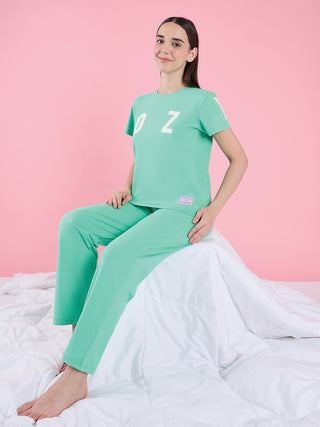 A woman poses wearing a green t-shirt with "OZ" printed in white and matching green pants.