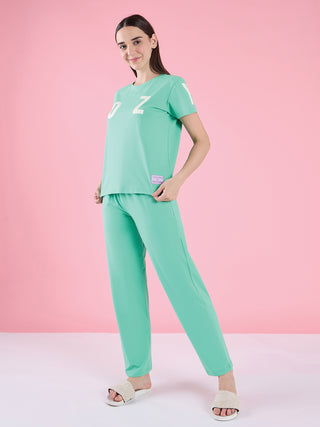 Women wearing a mint green pajama set with a "Cozy" graphic print on the top, standing with hands on hips.