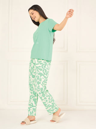 A woman stands in a playful pose wearing a mint green t-shirt with a graphic print and matching mint green pajama pants with a white abstract pattern.