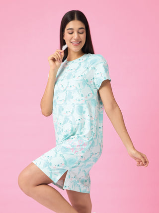 A woman in a pale blue printed nightgown with a koala pattern poses against a pink backdrop, holding a feather.