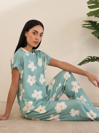 A woman in a teal floral pajama set with white flowers and lace trim.
