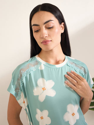 A woman in a light blue, floral print sleep shirt with lace accents, placing her hand on her chest.