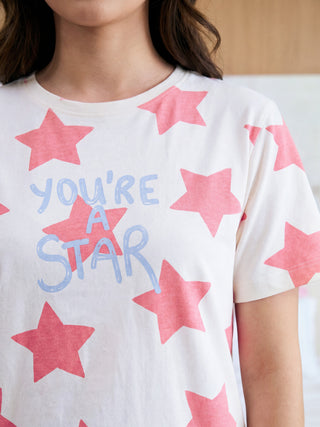 A woman models a comfortable cream short-sleeved tee, adorned with scattered coral stars and a light blue "YOU'RE A STAR" graphic across her chest.