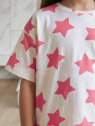 A child wears a white short-sleeved pajama top with an all-over pink star print, seen from the back-side.
