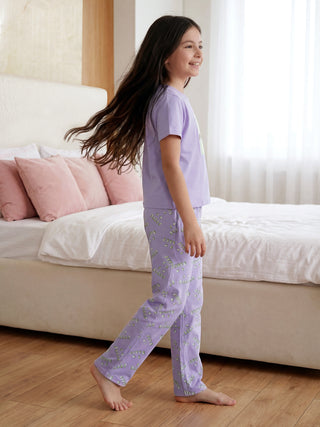 A happy young girl with long, flowing hair walks, wearing a lavender two-piece pajama set with a repeating "SLEEP" print on the pants.