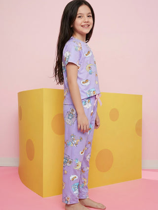 A smiling girl stands slightly turned, wearing a light purple short-sleeved and long-legged pajama set with a dreamy print of cartoon mice, cats, clouds, and stars.