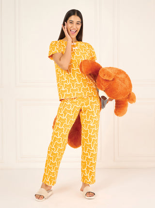 A woman poses playfully in a yellow pajama set with a white bear print, holding a large stuffed animal.