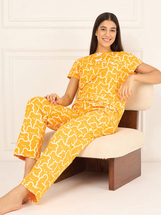 A young woman wearing a yellow and white bear-print pajama set and light pink slippers sits on a chair with her legs crossed.