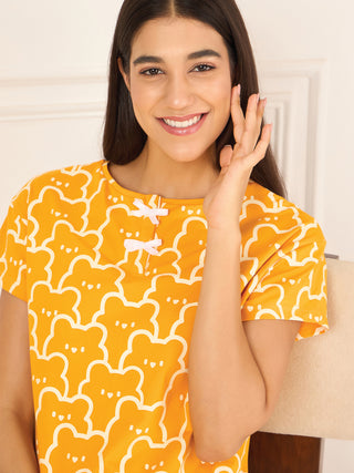 A woman in a yellow pajama top with a white bear print is smiling and touching her face.