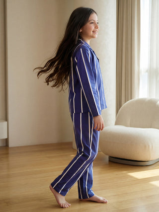 A smiling young girl with long, flowing hair walks in a two-piece blue pajama set featuring white vertical stripes.