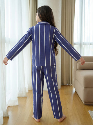 A young girl, seen from the back with arms outstretched, wears navy blue sleepwear with crisp white vertical stripes.