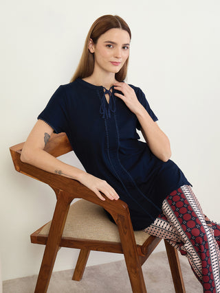 A woman sits on a wooden chair wearing a navy blue top and patterned leggings.