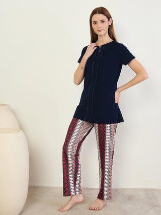 A woman stands wearing a navy blue top with decorative ties and patterned leggings with a red, cream, and black geometric print.