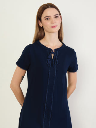 A woman in a navy blue tie-neck t-shirt dress with embroidered trim.