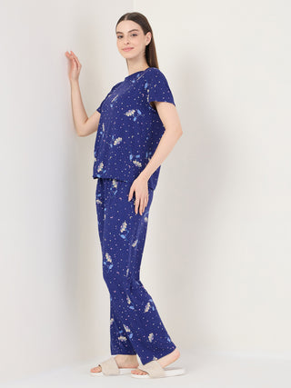 Women in a navy blue pajama set with a celestial floral print, posing standing and leaning against a wall.