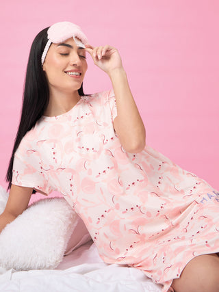 A woman poses wearing a pink, short-sleeved sleep dress with a playful bunny print.